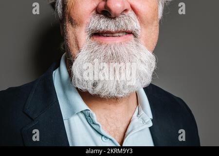 Rognez la moitié de la vue d'un homme à poil gris vieilli dans des vêtements élégants debout sur fond gris Banque D'Images
