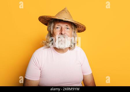 Portrait d'un homme âgé aux cheveux gris en t-shirt rose et chapeau de paille regardant l'appareil photo et souriant Banque D'Images