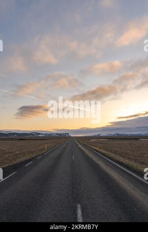 Vue en perspective d'une route asphaltée vide traversant le champ avec de l'herbe sèche contre un ciel nuageux à Vik, en Islande Banque D'Images