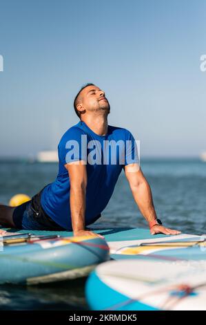 Calme adulte homme faisant face au chien yoga poser sur le paddleboard tout en pratiquant dans l'eau de mer Banque D'Images