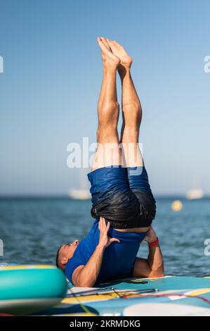 Homme plein corps en short humide faisant appui sur l'épaule tout en équilibrant sur le paddleboard dans l'eau de mer le jour ensoleillé Banque D'Images