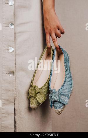 Femme méconnaissable en robe en coton décontractée portant des chaussures élégantes de différentes couleurs sur un mur gris Banque D'Images