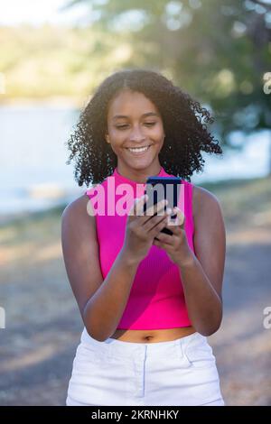 Belle fille souriante avec une coiffure bouclés à l'aide d'un smartphone pendant une journée d'été Banque D'Images