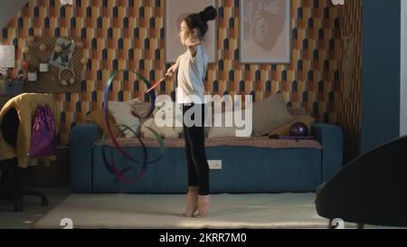 Une jeune fille asiatique danse avec un ruban de gymnastique, montrant la fente verticale des jambes et tourne autour d'elle. Entraînement de gymnastique. Loisirs sportifs. Mise à niveau de la santé physique en quarantaine. Ralenti. Banque D'Images