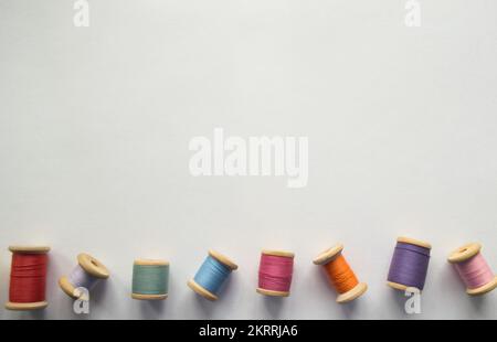 Beaucoup de fils multicolores sur des rouleaux en bois à l'ancienne sur un fond blanc avec un espace pour le texte. L'un des rouleaux de filetage est vide. Banque D'Images