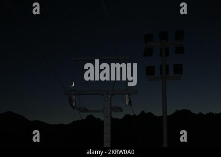 Infrastructure de télécabine avec projecteurs éteints sur la montagne suisse la nuit silhoueté contre le ciel bleu de gradient d'heure avec croissant de lune Banque D'Images