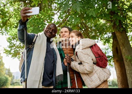 Groupe d'amis souriants prenant le selfie dans la nature tout en appréciant la randonnée ensemble Banque D'Images