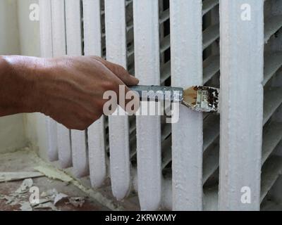 peinture de vieux radiateurs en fer dans une pièce en cours de rénovation, à l'aide d'une brosse à long manche lors de la peinture de radiateurs de chauffage dans un appartement, un radiateur d'époque Banque D'Images