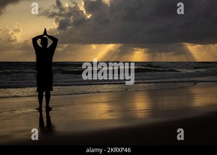 Silhouette d'un homme pratiquant le yoga au lever du soleil sur la plage Banque D'Images