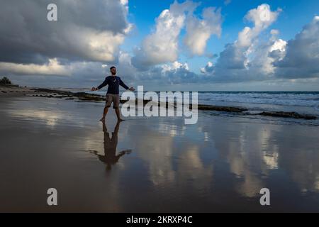 Hipster regardant un homme blanc d'âge moyen sur la plage qui fait du yoga au lever du soleil. Banque D'Images