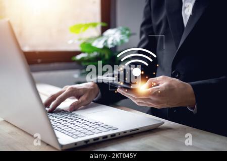 Main d'homme d'affaires utilisant un smartphone avec symbole wi-fi et un ordinateur portable à saisie de mains (ordinateur portable). Technologie d'entreprise lien numérique concept. Banque D'Images