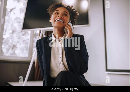 Une femme joyeuse qui parle sur un smartphone au bureau Banque D'Images