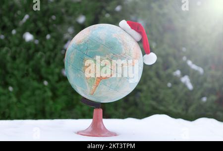 globe avec chapeau de noël sur la neige. Chapeau de père Noël bokeh FLARE comme concept de voyage Banque D'Images