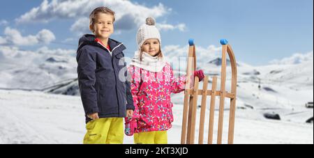 Garçon et fille en vêtements d'hiver debout avec un traîneau en bois sur une montagne enneigée Banque D'Images