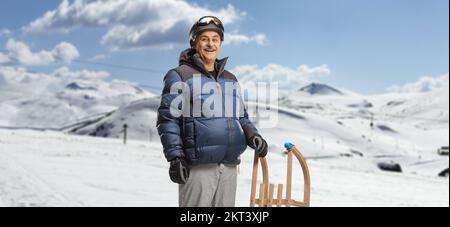 Homme mature en vêtements d'hiver debout avec un traîneau en bois sur une station de ski de montagne Banque D'Images