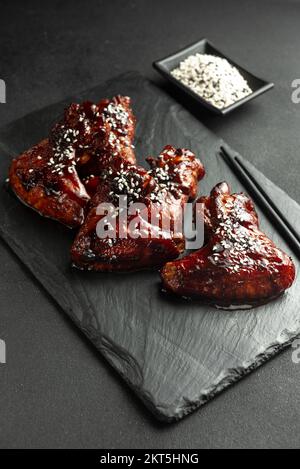 Ailes de poulet de style asiatique en sauce aigre-douce sur une assiette sur fond de pierre sombre avec espace à copier. Vue de dessus, plan plat Banque D'Images