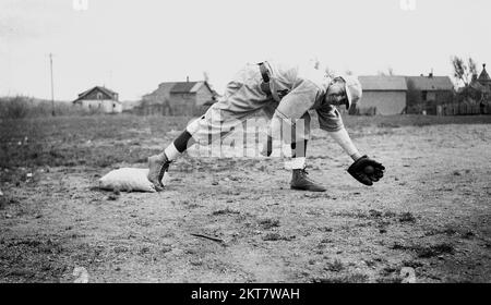 1934, historique, à l'extérieur dans un champ de terre, un écolier dans l'équipement de baseball de l'époque, avec un gant de baseball incliné vers le haut pour attraper une balle, Mapplewood Grammar School, États-Unis. Banque D'Images