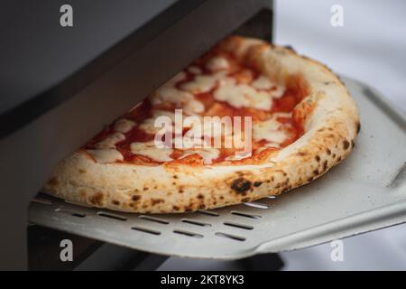 Cuisson ou cuisson de pizza chaude Margherita avec sauce tomate et mozzarella avec une pelle dans un four électrique ou à gaz, avec fumée, gros plan Banque D'Images