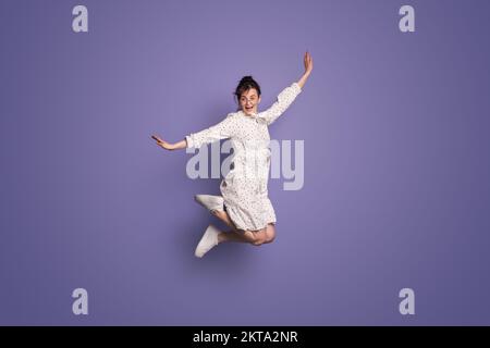 Photo de la taille du corps de la jolie fille qui se porte en robe tout en sautant isolé sur fond violet. Des gens heureux émotions positives Banque D'Images