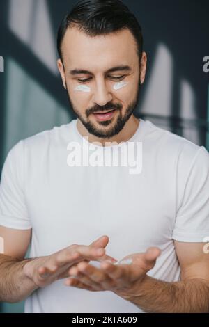 Homme prenant soin de ses rides undereye mettant anti vieillissement hydratant pour les yeux. Soin du visage. Portrait de beauté. Produit de beauté. Soins de la peau anti-âge Banque D'Images