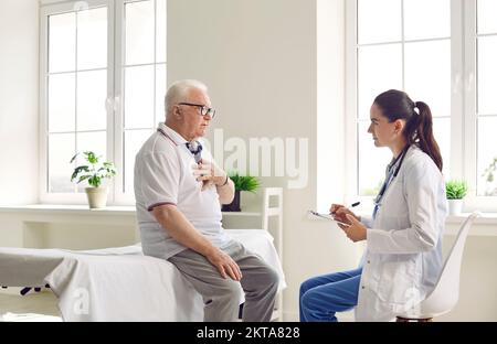 Un homme âgé agité avec des lunettes tient sa main sur sa poitrine, parlant à un médecin en manteau blanc. Banque D'Images