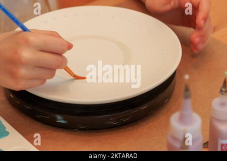 Un enfant peint et décorera artistiquement une assiette Banque D'Images