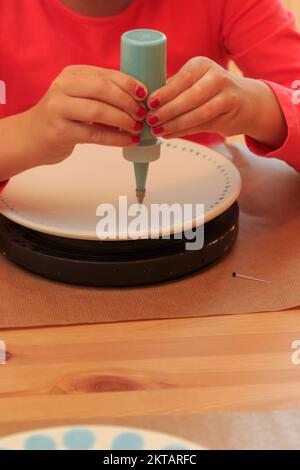 Un enfant peint et décorera artistiquement une assiette Banque D'Images