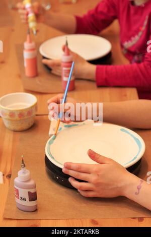 Un enfant peint et décorera artistiquement une assiette Banque D'Images