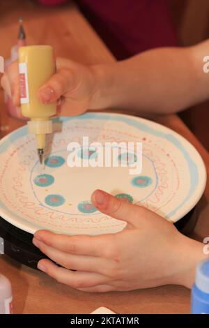 Un enfant peint et décorera artistiquement une assiette Banque D'Images