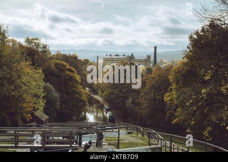 2 personnes près des portes d'écluses, bateaux amarrés, moulin Damart éclairé au soleil, couleur automnale - Bingley Five Rise Locks, Leeds & Liverpool Canal, West Yorkshire Angleterre Royaume-Uni. Banque D'Images