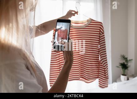 Femme prenant photo d'un t-shirt rayé sur un smartphone. Banque D'Images