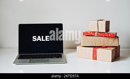 Vente en ligne, vacances achats en ligne, E-Commerce. Écran d'affichage d'ordinateur portable ouvert avec vente de mot et boîtes-cadeaux sur table blanche. Banque D'Images