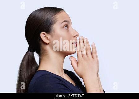 Jeune femme pleurait, tenant les mains dans la prière sur fond blanc, vue de profil Banque D'Images