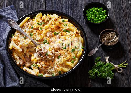 Thon Mornay, crémeux Thon Casserole Penne Pasta Bake dans un plat à pâtisserie sur une table en bois sombre avec une cuillère Banque D'Images