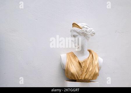 Buste antique de tête de femme contre le mur gris. Statue historique en robe dorée. Visage de femme antique sur fond clair. Photo de haute qualité Banque D'Images