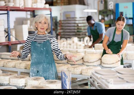 Portrait d'un artisan âgé parmi des assiettes et des tasses en céramique dans l'atelier de poterie Banque D'Images