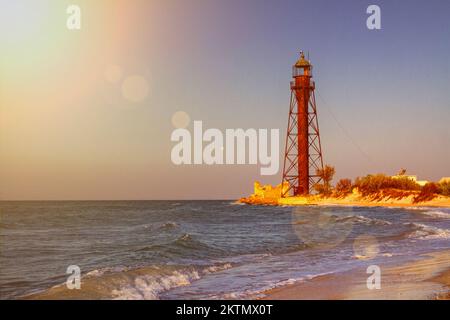 Vieux phare abandonné rouillé sur la côte de la mer au lever du soleil près des ruines sur la plage de sable Banque D'Images