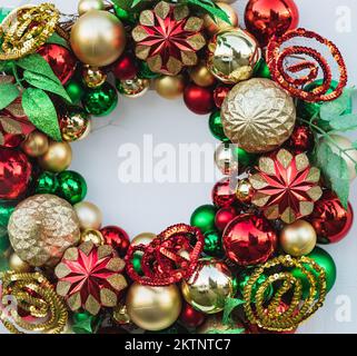 Couronne de Noël décorée de boules dorées et rouges, lumières, isolée sur blanc. Couronne de Noël accrochée à la porte blanche. Personne, attention sélective Banque D'Images