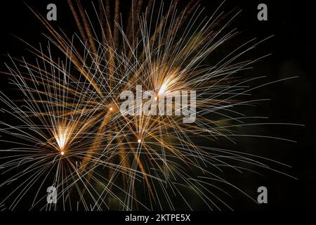 Feux d'artifice blancs, dorés et jaunes sur fond de ciel noir la nuit. Banque D'Images