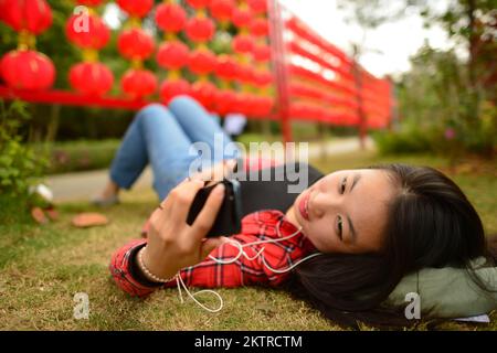 Une femme chinoise utilise un smartphone dans le parc pendant le nouvel an chinois Banque D'Images