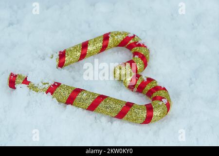 Cannes de bonbon pailletées rouge doré sur la neige blanche. Banque D'Images