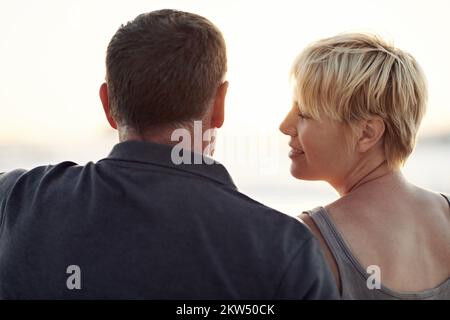 Prendre un beau coucher de soleil. Un couple aimant assis sur la plage - vue arrière. Banque D'Images