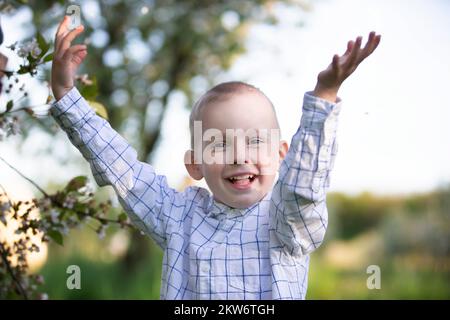 Un enfant heureux dans un jardin de printemps en pleine floraison se réjouit, sourit. Banque D'Images