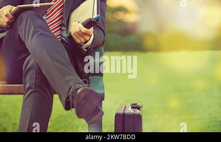 Faire des affaires dans le parc. un homme d'affaires assis sur un banc de parc avec sa tablette numérique et son organiseur. Banque D'Images