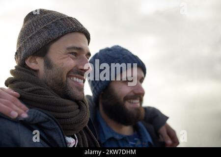 Enveloppé dans le froid de l'océan. Deux beaux jeunes pêcheurs se tenant sur la plage un matin frais. Banque D'Images