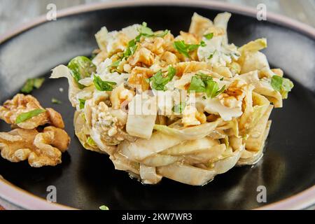 Salade de chicorée endive avec sauce Roquefort sur une assiette noire. Pose à plat. Gros plan. Banque D'Images