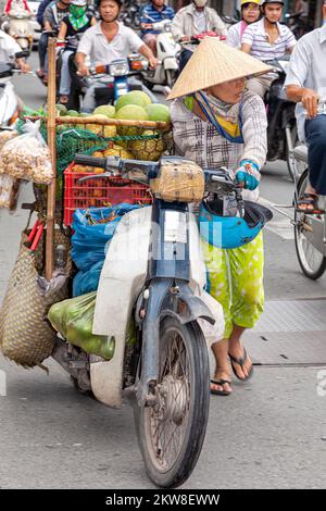 Un motard vietnamien portant un chapeau de bambou vendant des fruits de moto, Ho Chi Minh ville, Vietnam Banque D'Images