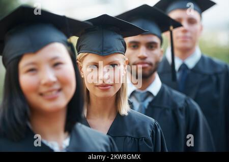 Prêt pour le monde réel. Les jeunes diplômés de l'université détiennent leurs diplômes tout en restant dans une rangée. Banque D'Images