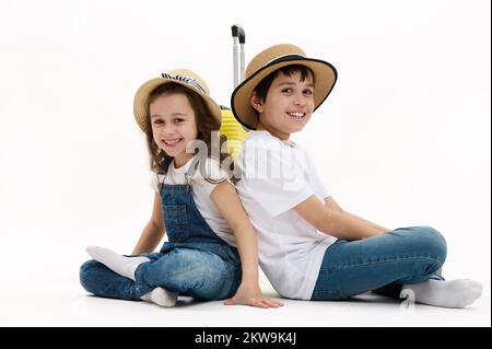 Les enfants adorables, frère et sœur s'assoient avec leur dos les uns aux autres dans la posture du lotus, sourient sur l'appareil photo, sur fond blanc Banque D'Images