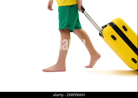 Short d'été vert avec valise jaune, pieds nus sur fond blanc Banque D'Images